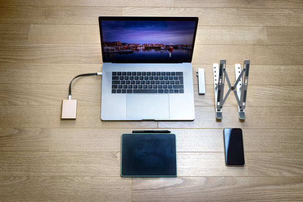 Top view of a laptop with a drawing graphic tablet, a mobile phone, a foldable stand, a ssd hard disk and a hub type C adapter - Photo, Image