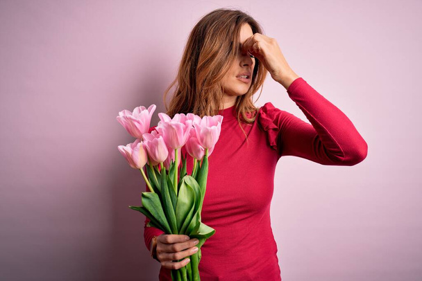 Young beautiful brunette woman holding bouquet of pink tulips over isolated background tired rubbing nose and eyes feeling fatigue and headache. Stress and frustration concept. - Φωτογραφία, εικόνα