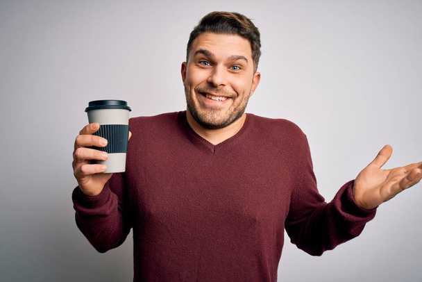 Young man with blue eyes drinking coffee from take away plastic bottle over isolated background very happy and excited, winner expression celebrating victory screaming with big smile and raised hands - Photo, image