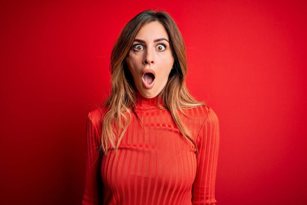 Young beautiful brunette woman wearing casual turtleneck sweater over red background afraid and shocked with surprise and amazed expression, fear and excited face. - Fotografie, Obrázek