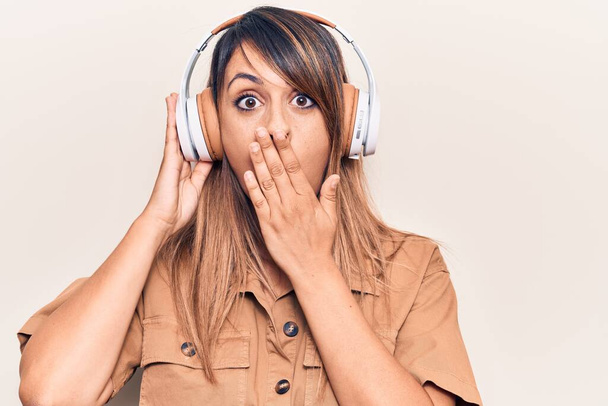 Young beautiful woman listening to music using headphones covering mouth with hand, shocked and afraid for mistake. surprised expression  - Фото, зображення
