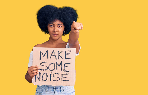 Young african american girl holding make some noise banner pointing with finger to the camera and to you, confident gesture looking serious  - Photo, Image