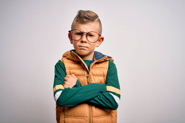 Ein kleines kaukasisches Kind mit blauen Augen, Wintermantel und smarter Brille, skeptisch und nervös, mit missbilligendem Gesichtsausdruck und verschränkten Armen. Negative Person. - Foto, Bild