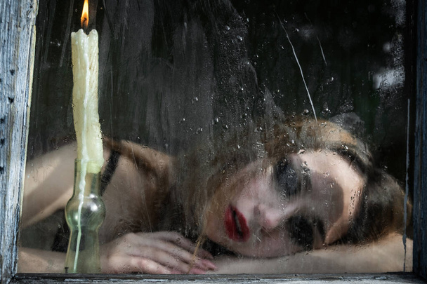 Beautiful sad young girl looking out the window with a candle, good for book cover - Foto, imagen