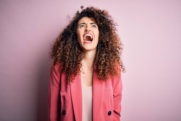 Young beautiful businesswoman with curly hair and piercing wearing elegant jacket angry and mad screaming frustrated and furious, shouting with anger. Rage and aggressive concept. - Foto, afbeelding