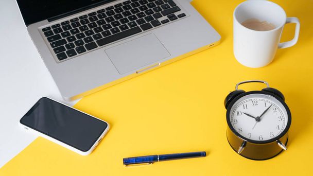 Background - Yellow business man working table in modern office and cup of coffee, clock, smartphone, pen, laptop. - Fotó, kép