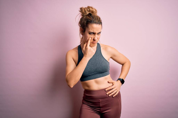 Young beautiful blonde sportswoman doing sport wearing sportswear over pink background Pointing to the eye watching you gesture, suspicious expression - Photo, image