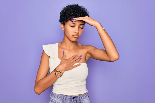 Young beautiful african american afro woman wearing casual t-shirt over purple background Touching forehead for illness and fever, flu and cold, virus sick - Photo, image