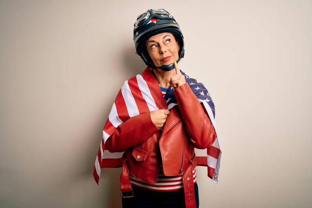 Middelbare leeftijd motorrijder vrouw het dragen van motorfiets helm en Verenigde Staten vlag ernstige gezicht denken over de vraag, zeer verward idee - Foto, afbeelding