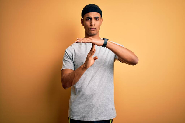 Schöner afrikanisch-amerikanischer Sportler, der Sport in Sportbekleidung über gelbem Hintergrund macht Auszeit Geste mit Händen, frustriertem und ernstem Gesicht - Foto, Bild