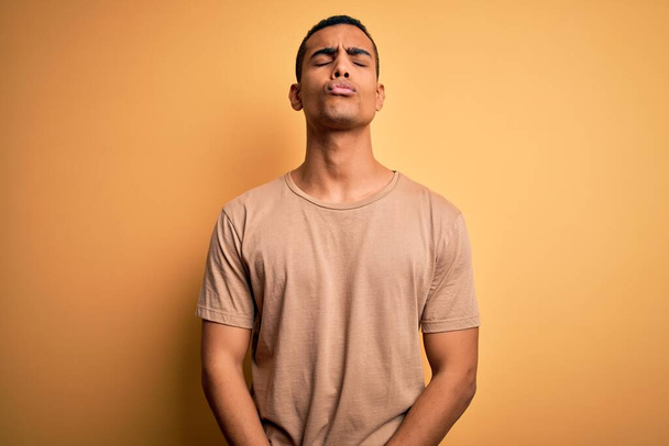 Young handsome african american man wearing casual t-shirt standing over yellow background looking at the camera blowing a kiss on air being lovely and sexy. Love expression. - Foto, Bild