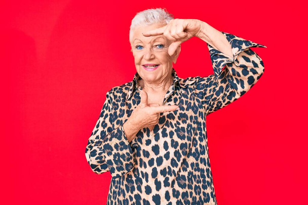 Ältere schöne Frau mit blauen Augen und grauen Haaren trägt lässig und modern Leoparden-Animal-Print-Shirt lächelnd Rahmen mit Händen und Fingern mit glücklichem Gesicht. Kreativität und Fotografiekonzept.  - Foto, Bild