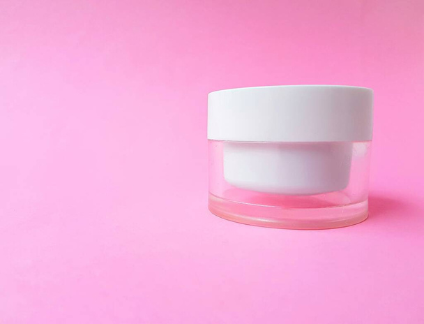 Transparent jar with cream and white lid on a bright pink background. Space for text. - Foto, immagini