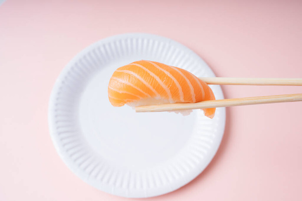 Свіжі суші лосося на білій тарілці, що їдять з паличкою на рожевому фоні
. - Фото, зображення