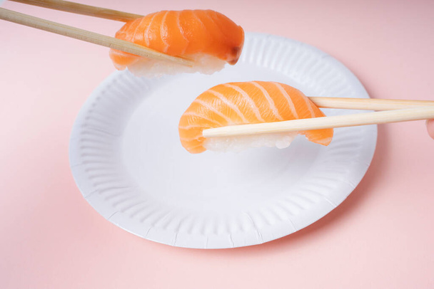 Φρέσκο σούσι σολομού σε λευκό πιάτο τρώγοντας με ξυλάκια σε ροζ φόντο. - Φωτογραφία, εικόνα