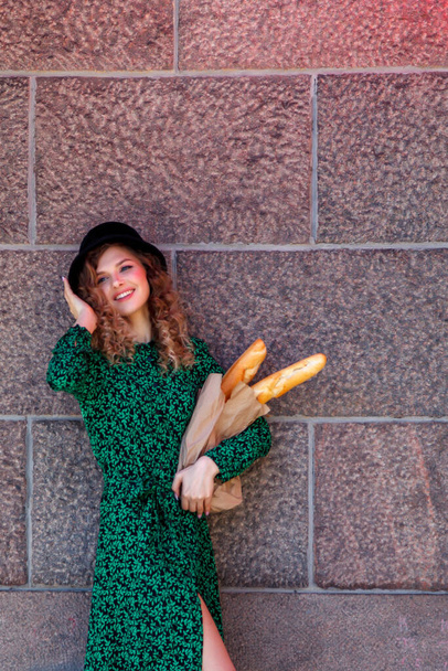 Portrait woman dressed in French style with baguette in hand. French style of Paris. Close-up of French woman in stylish clothes holding fresh baguettes and smiling. Place for an inscription or logo - Foto, Bild