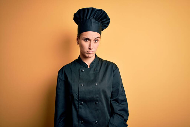 Young beautiful chef woman wearing cooker uniform and hat standing over yellow background skeptic and nervous, frowning upset because of problem. Negative person. - Foto, Imagem