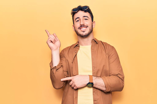 Giovane uomo ispanico indossa abiti casual sorridente felice indicando con mano e dito di lato  - Foto, immagini