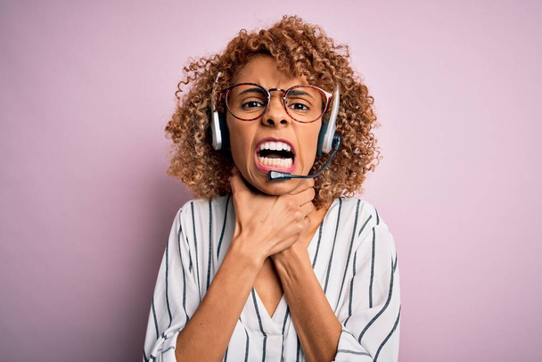 Afroamerikanisch lockige Callcenter-Agentin arbeitet mit Headset über rosa Hintergrund schreien und ersticken, weil qualvolle Würgen. Gesundheitsprobleme. Asphyxid- und Selbstmordkonzept. - Foto, Bild