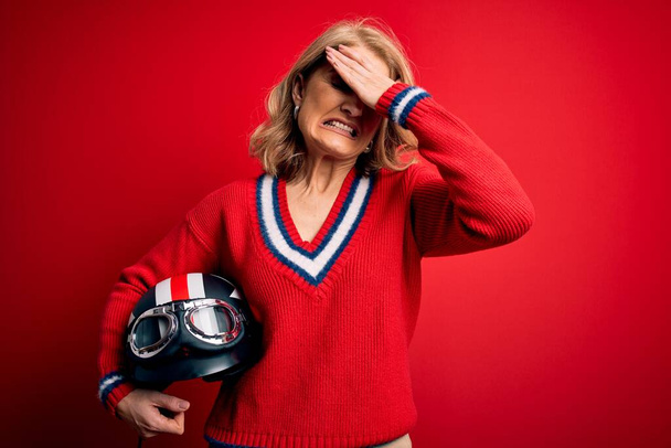 Medioevo bella donna motociclista bionda che tiene il casco moto su sfondo rosso stressato con mano sulla testa, scioccato con vergogna e faccia a sorpresa, arrabbiato e frustrato. Paura e sconvolto per errore. - Foto, immagini