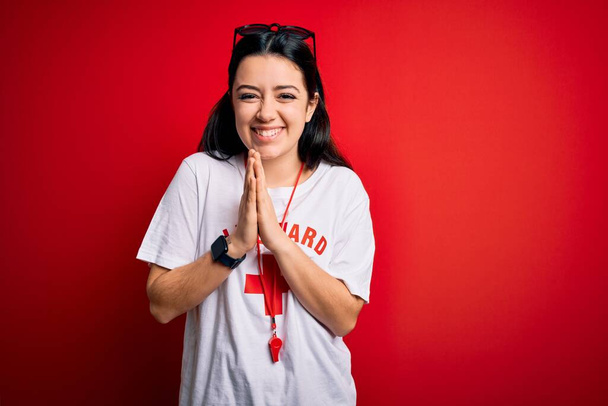 Young lifeguard woman wearing secury guard equipent over red background praying with hands together asking for forgiveness smiling confident. - Photo, Image