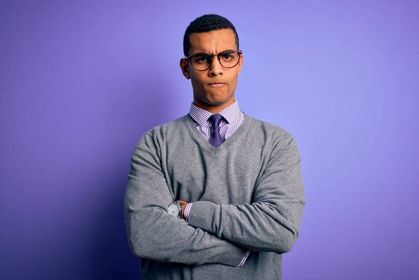 アフリカ系アメリカ人のビジネスマンが眼鏡をかけ、紫色の背景に懐疑的で緊張した顔をしており、両腕を組んで反対意見の表明をしていない。負の人. - 写真・画像