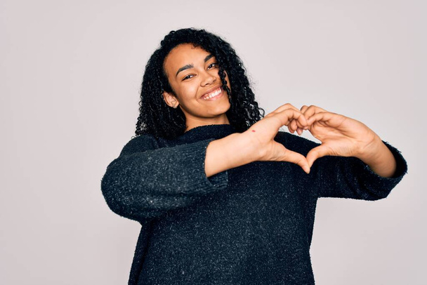 Young african american curly woman wearing casual sweater standing over white background smiling in love showing heart symbol and shape with hands. Romantic concept. - Photo, Image