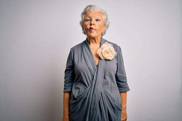 Ältere schöne grauhaarige Frau in lässigem Kleid steht vor weißem Hintergrund und macht Fischgesicht mit Lippen, verrückte und komische Geste. Lustiger Ausdruck. - Foto, Bild