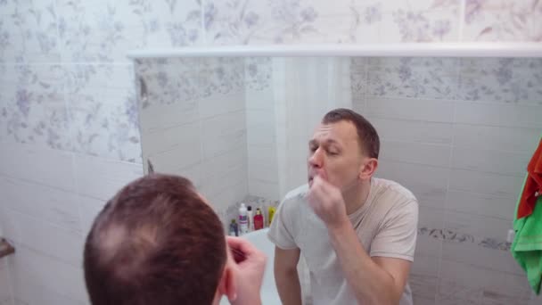 Ένας άντρας βγάζει μια τρίχα από τη μύτη του, στέκεται στο μπάνιο μπροστά από έναν καθρέφτη, φροντίζοντας τον εαυτό του. - Πλάνα, βίντεο