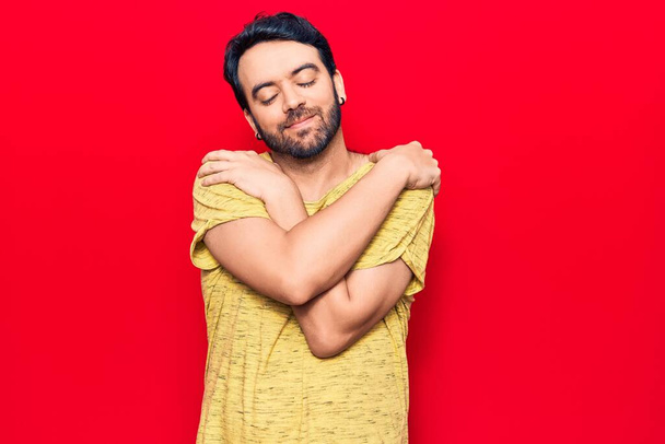 Nuori latinomies yllään rento vaatteita halaamalla itseään onnellinen ja positiivinen, hymyillen luottavainen. itserakkaus ja itsehoito  - Valokuva, kuva
