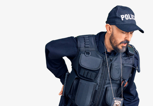 Jonge knappe man draagt politie-uniform lijden aan rugpijn, raken rug met de hand, spierpijn  - Foto, afbeelding