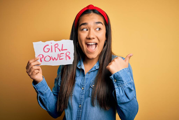 Junge schöne asiatische Frau trägt Diadema mit Banner mit Girl Power Botschaft zeigt und zeigt mit dem Daumen zur Seite mit glücklichem Gesicht lächelnd - Foto, Bild