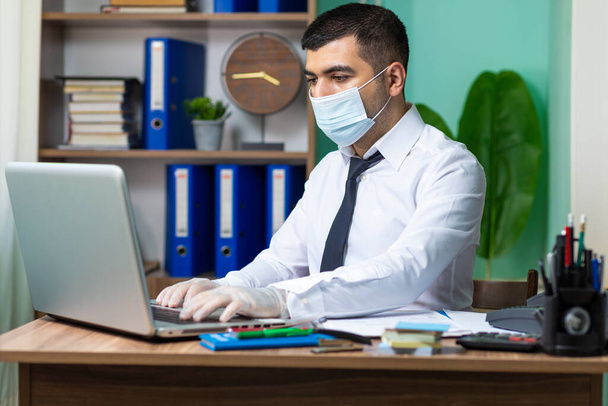 Young business man working on laptop with medical protective mask and gloves - Photo, Image