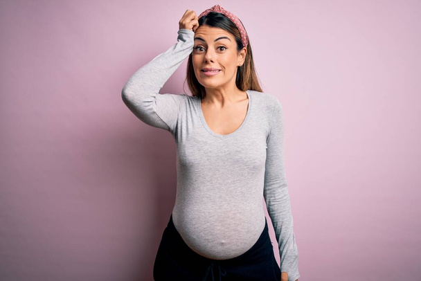 Young beautiful brunette woman pregnant expecting baby over isolated pink background confuse and wonder about question. Uncertain with doubt, thinking with hand on head. Pensive concept. - Fotoğraf, Görsel
