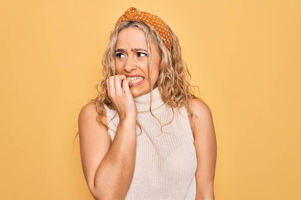 Schöne blonde Frau in lässigem T-Shirt und Diadem über isoliertem gelbem Hintergrund, die gestresst und nervös mit Händen auf mundgebissenen Nägeln aussieht. Angstproblem. - Foto, Bild