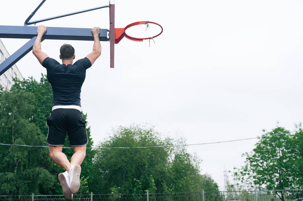 The fitness coach pulls up on the basketball basket crossbar. The concept of exercise on pectoral muscles in the fresh air - Fotoğraf, Görsel