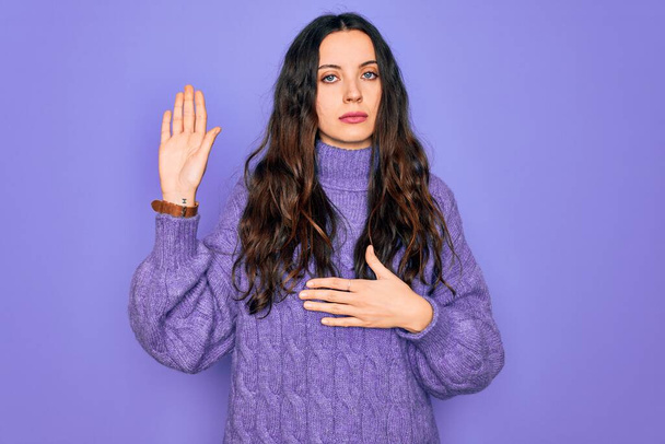 Young beautiful woman wearing casual turtleneck sweater standing over purple background Swearing with hand on chest and open palm, making a loyalty promise oath - Fotó, kép