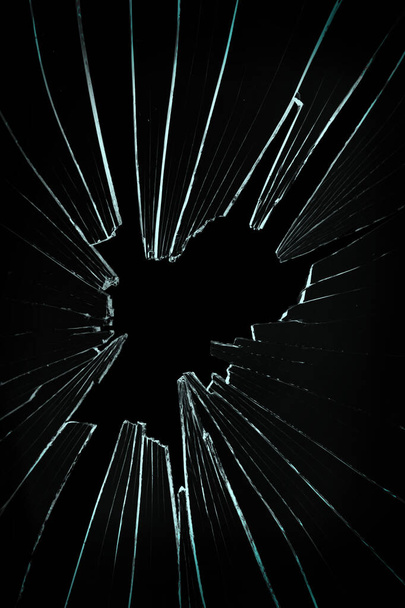 Η τρύπα στο σπασμένο και ραγισμένο γυαλί σε μαύρο φόντο - Φωτογραφία, εικόνα