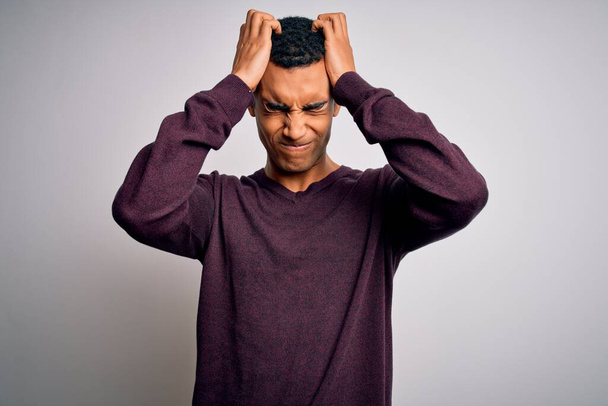 Jonge knappe Afro-Amerikaanse man draagt casual trui over witte achtergrond die lijdt aan hoofdpijn wanhopig en gestrest omdat pijn en migraine. Handen op het hoofd. - Foto, afbeelding