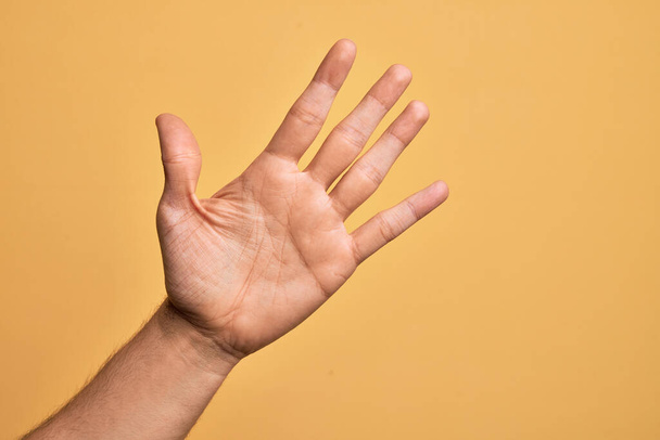 Hand of caucasian young man showing fingers over isolated yellow background counting number 5 showing five fingers - Фото, изображение