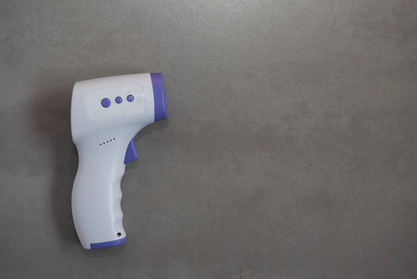 Infrared thermometer lies on grey background. Pandemic. Social distancing. Virus protection concept. Copy space - 写真・画像