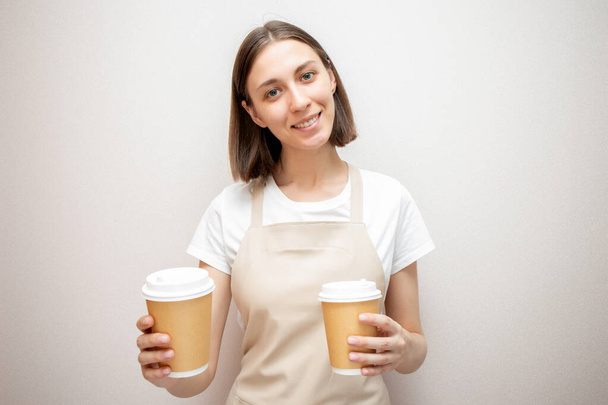 Smiling barista wearing apron holding two paper cups. - Foto, immagini