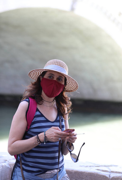Jeune femme avec masque chirurgical et chapeau de paille en voyage dans la ville - Photo, image