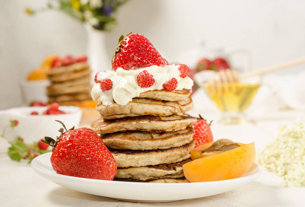 A stack of pancakes with whipped cream, strawberries and fruit close-up. Tasty summer breakfast. Food photo. - 写真・画像