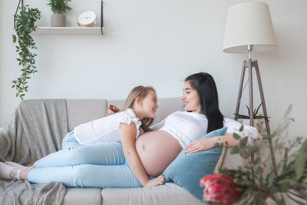 妊娠中の母親と娘を屋内で。子供と母親は新生児を待っている。幸せな家族の期待. - 写真・画像
