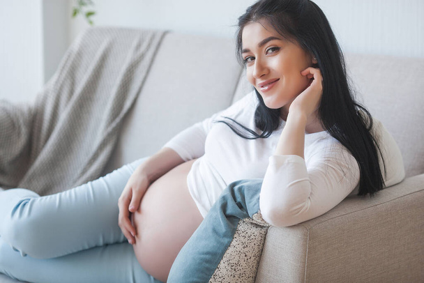 Attractive young woman expecting a child. Pregnant woman. Female indoors embracing her stomach. - Fotoğraf, Görsel