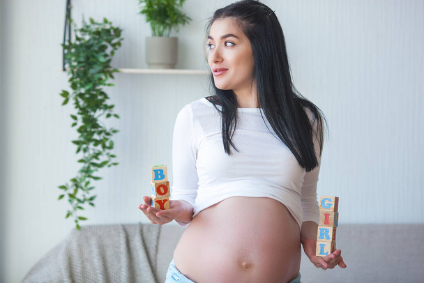 Pregnant woman holding an abc cubes with boy and girl words. Expecting female womdering about sex of her unborn baby. - Photo, Image