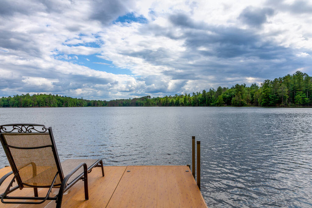 Beach chair on a dock in a Northwoods lake.  Ample copy space in sky if needed. - Photo, Image