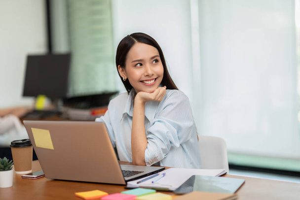Happy Asian business woman working with laptop and smile looking at camera at modern office or Co-Working Space,Business Startup Concept - Zdjęcie, obraz