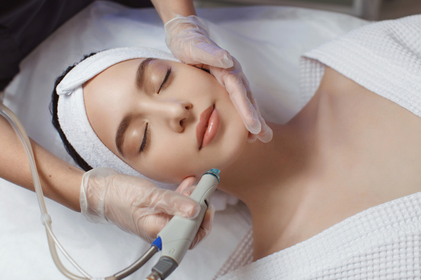 Вид збоку жінки, що отримує терапію мікродермабразією на лобі в косметичному спа-центрі
 - Фото, зображення